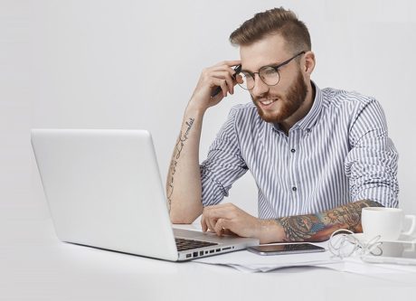 chico con tatuajes trabajando con su pc y móvil